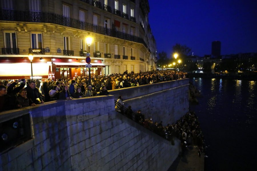 People watch Notre Dame cathedral burning from the Seine river banks in Paris, Monday, April 15, 2019. A catastrophic fire engulfed the upper reaches of Paris soaring Notre Dame Cathedral as it was undergoing renovations Monday, threatening one of the greatest architectural treasures of the Western world as tourists and Parisians looked on aghast from the streets below. (AP Photo/Francois Mori)